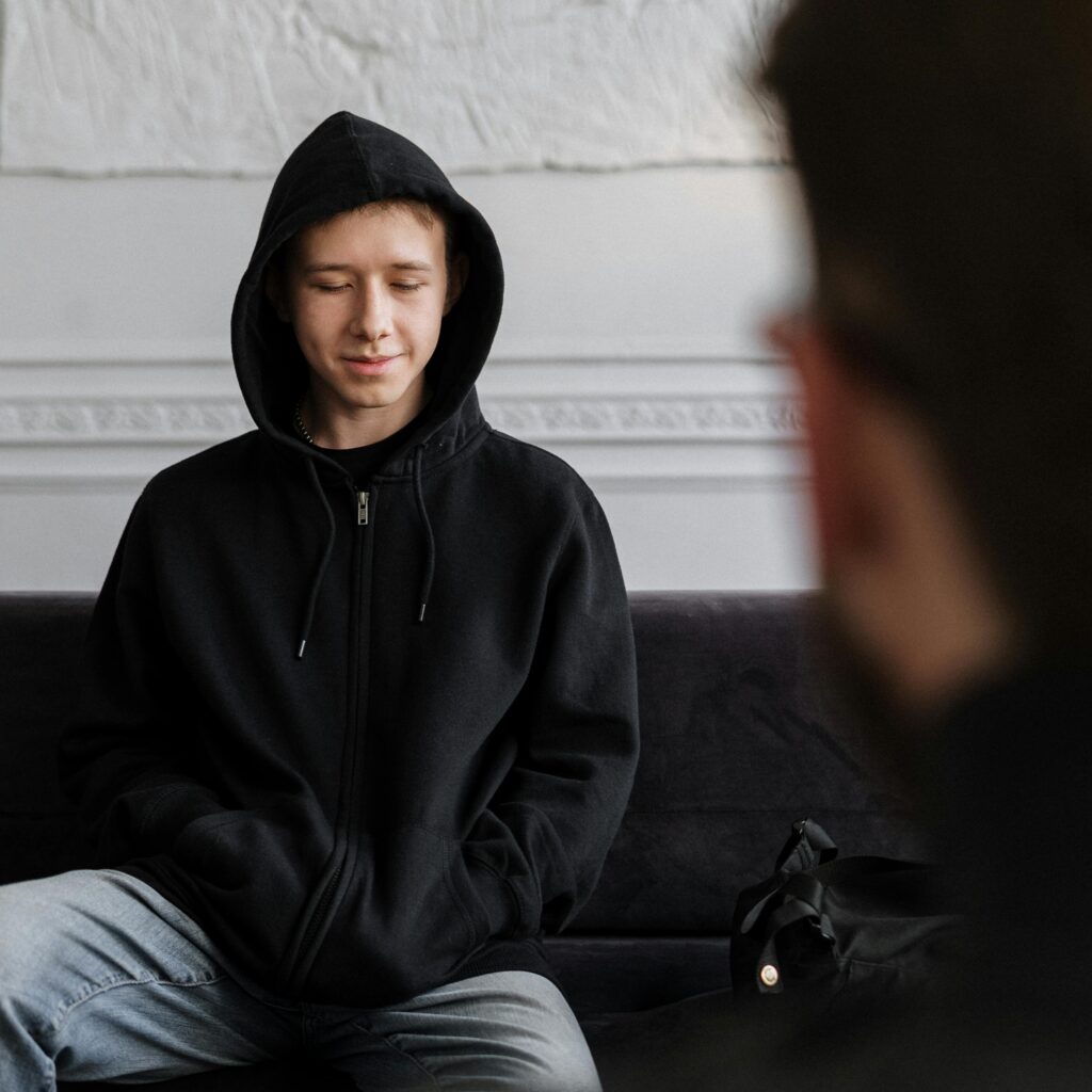 Mies istuu hupparissa sohvalla.